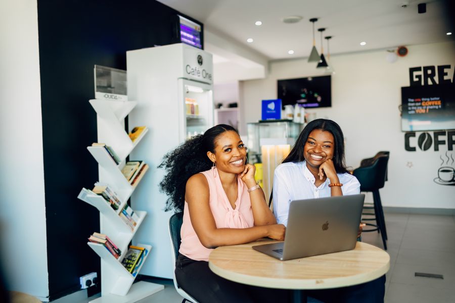 Two friends laughing over a laptop in a café