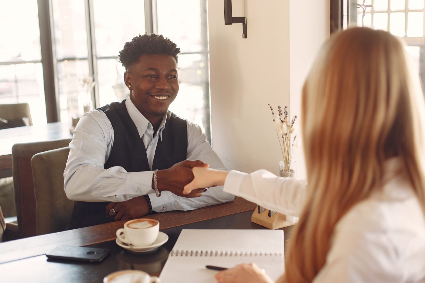 Two people smiling and shaking hands across a café table